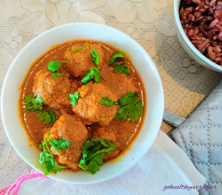 chicken meatballs in curry sauce in a ceramic bowl and a bowl of red rice