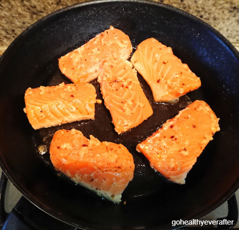 marinated pieces of orange butter salmon being fried in a pan
